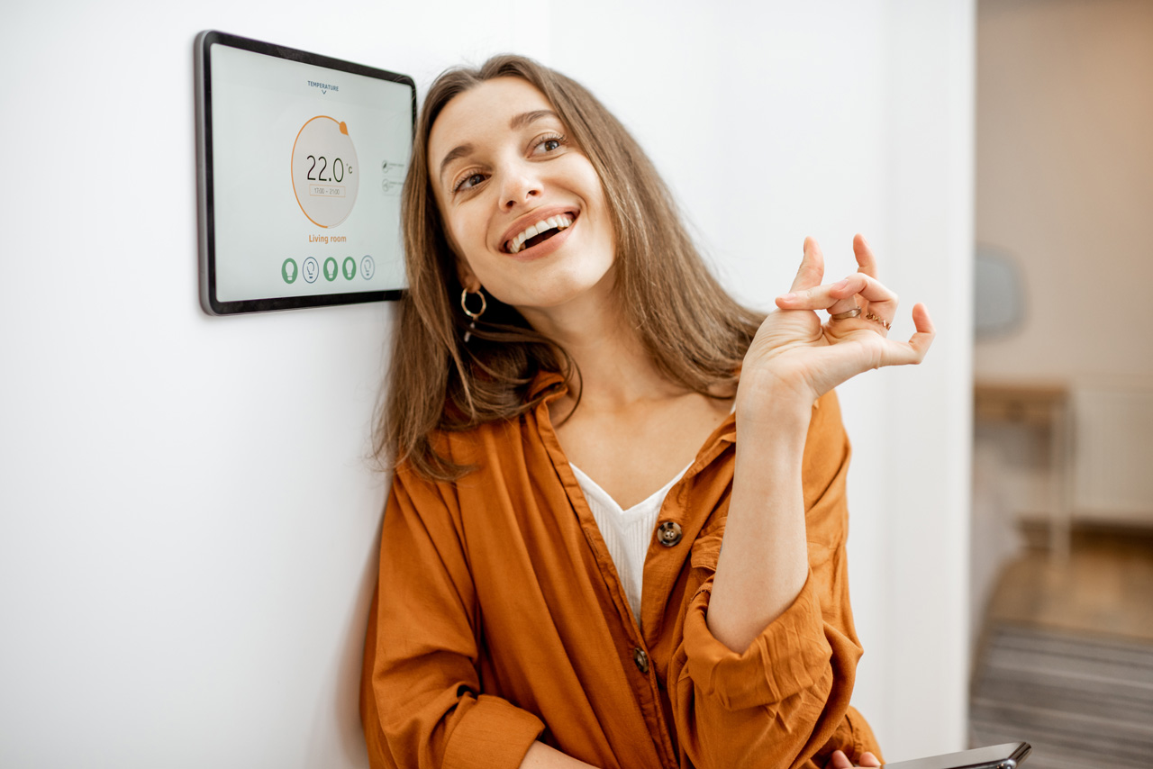 Portrait of a young happy woman near a touch screen panel for a smart home control. Concept of a simple and convenient application for managing smart devices at home