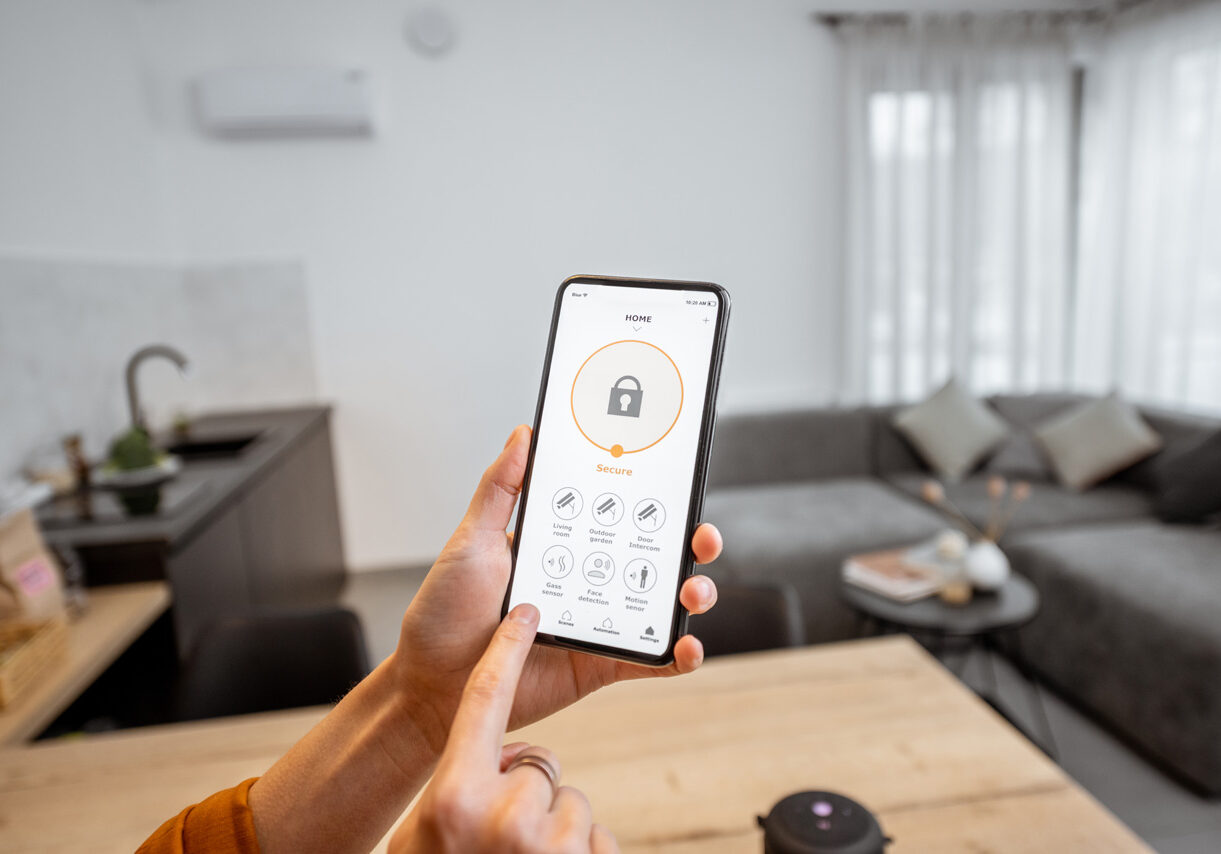 Holding a smartphone with launched security program indoors. Concept of controlling and managing home security from a mobile device