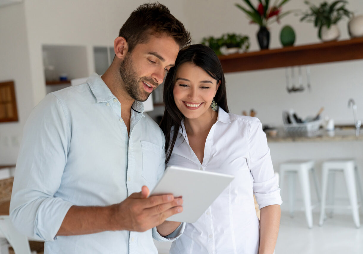 Portrait of a loving couple at home looking at social media on a digital tablet and smiling - lifestyle concepts